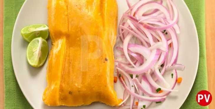 Imagen de un tamal peruano servido en un plato acompañado de salsa criolla o más conocida como sarsa criolla y su limón.