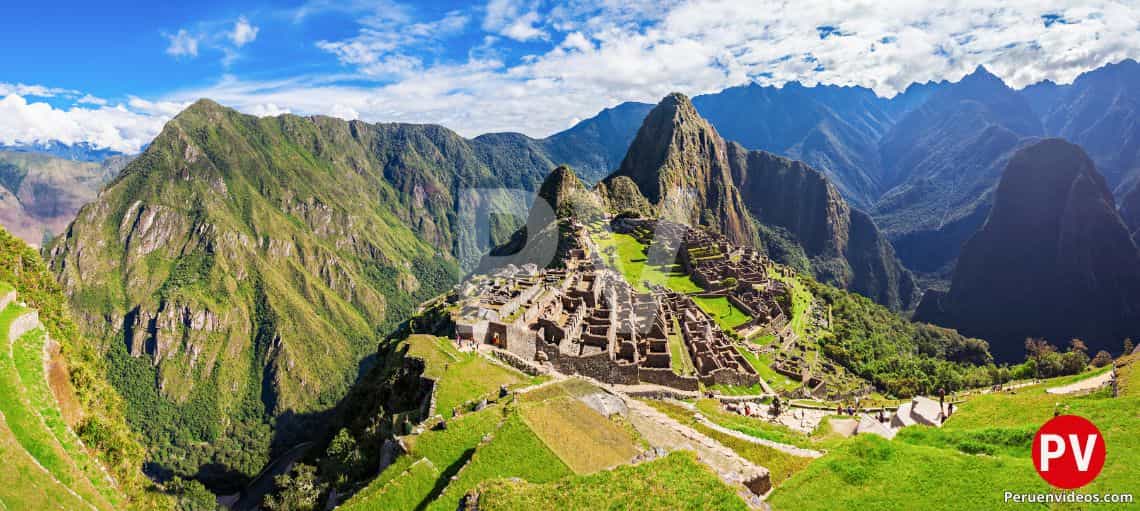 Vista de toda la ciudadela de machu Picchu con el Huayna Picchu atrás y rodeado de montañas cubiertas con nubes blancas.