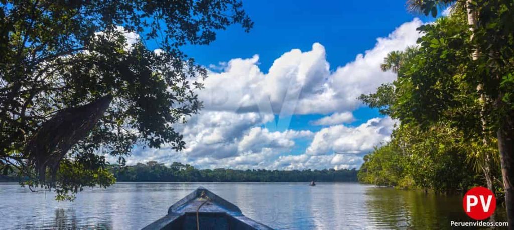 la punta de un bote con el lago Sandoval bajo él y al fondo la vegetación con nubes blancas muy espesas en el cielo.