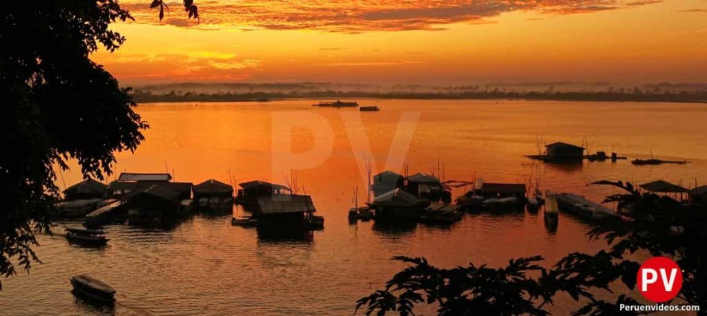 Río Amazonas en un atardecer, con casitas, canoas y botes en sus orillas.