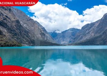 Montañas y nevados con densas nubes en su cima y un gran lago de aguas azules en sus faldas.